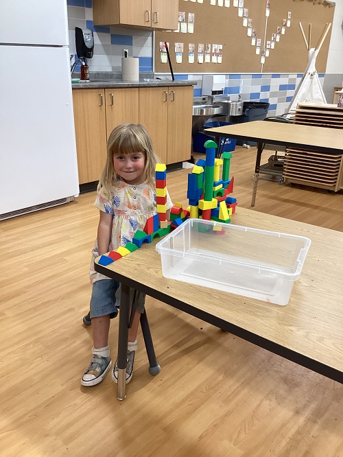 A child sitting with a structure they built with foam blocks.