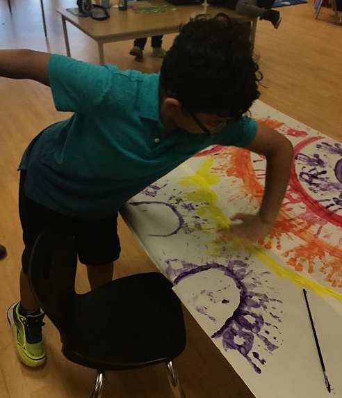 child adding a handprint to a painting of a rainbow