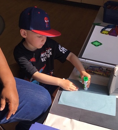 child applying glue from a glue stick onto a light blue piece of paper