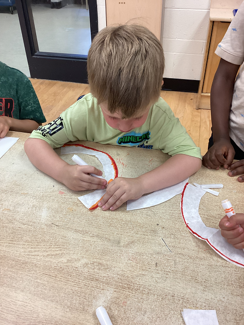 child sitting at a table looking down as he holds a marker and colours a rainbow