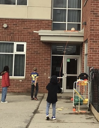children getting a ball off a roof using a hula hoop and a skipping rope