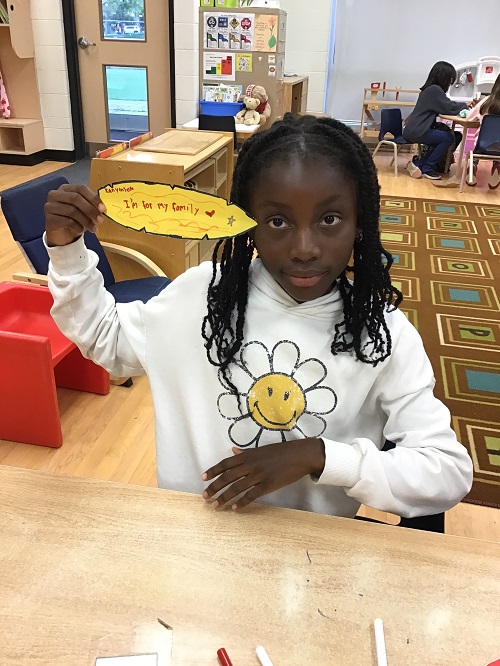 child holding a paper feather with what she is thankful for written on it