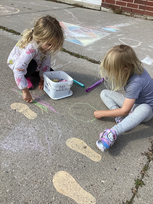 2 children sitting on the ground writting/drawing with chalk