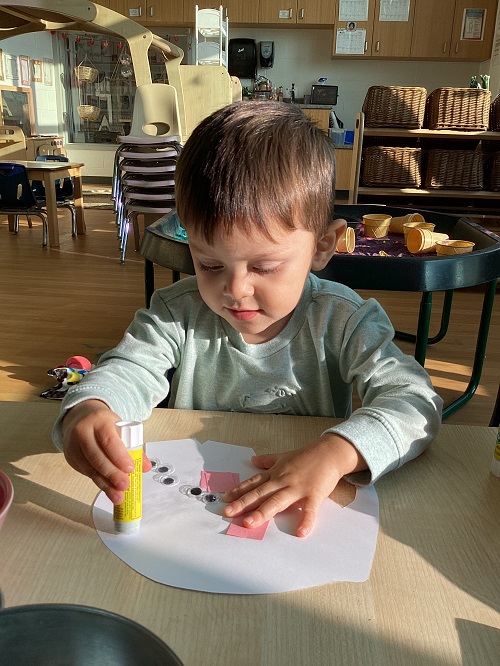 A preschool child gluing items to their Elmer elephant 