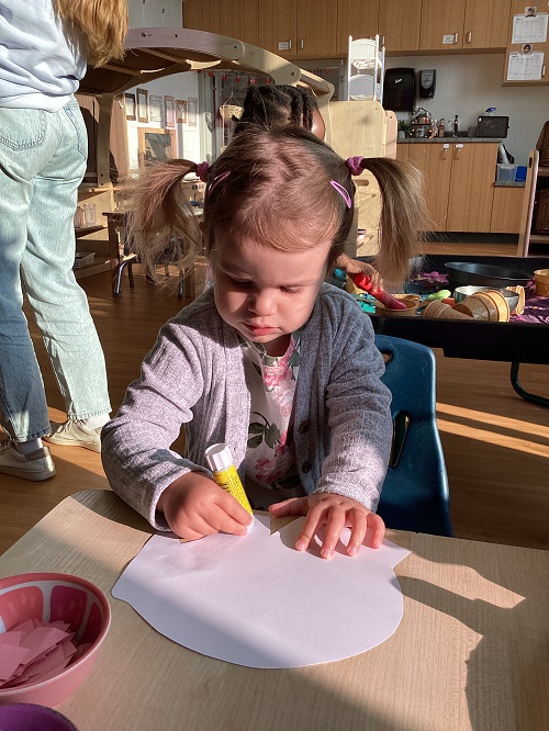 A preschool child gluing items to their Elmer elephant 