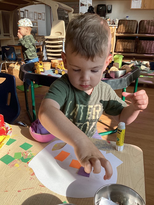 A preschool child gluing items to their Elmer elephant 