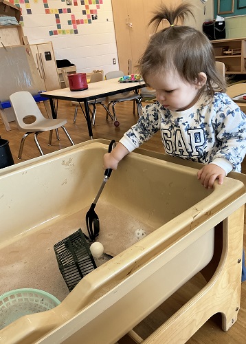 Toddler reaching into sensory bin for scoop