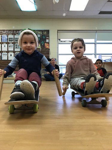 2 boys using sticks to push bodies on skateboards