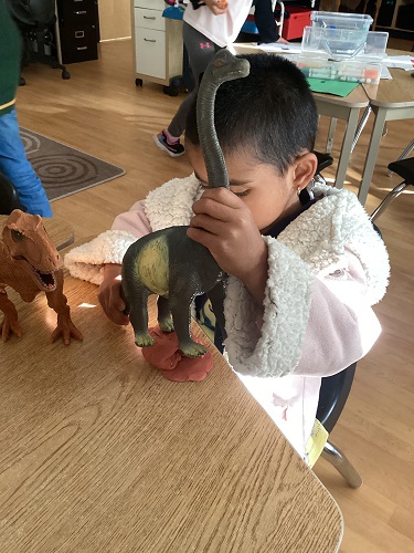 JK child holding a dinosaur with its feet on some clay