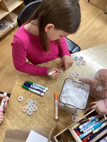 School Age 1 child sitting at the table with markers colouring on plastic bottle caps