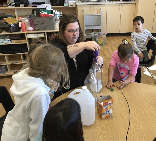 An educator attaching a balloon to a pop bottle while the children looked on