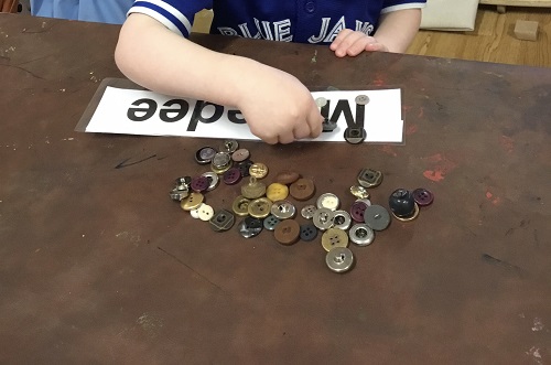 A name card on the table with a child's hand placing buttons on the letters