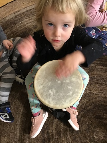 A child drumming on a drum in her lap