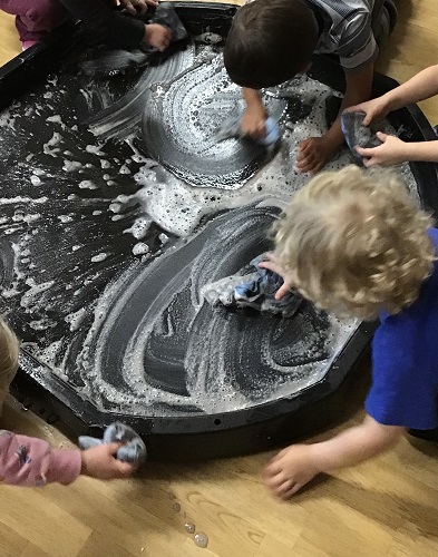 Children washing a tuff tray using soap, water and cloths