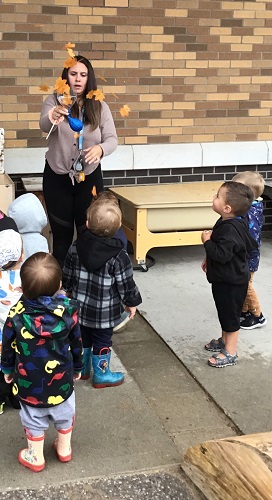 An educator and children throwing leaves into the air