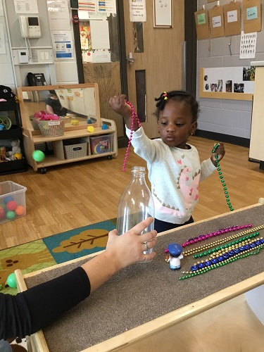 A child putting beads in and out of a plastic bottle