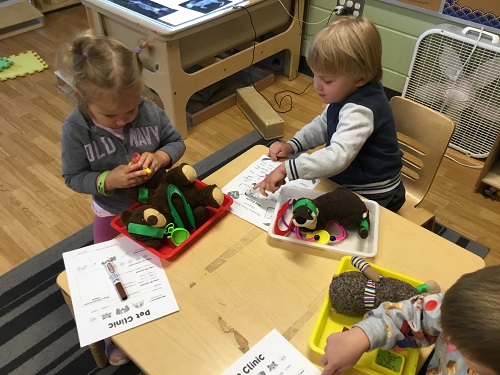 Children sitting at a table using vet instruments to take care of stuffed animals