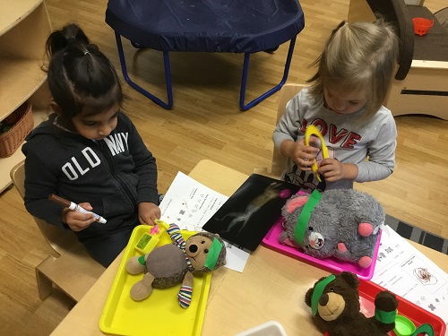 Two children sitting at a table using vet instruments to take care of stuffed animals