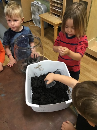 Children helping to scoop soil into a large jar