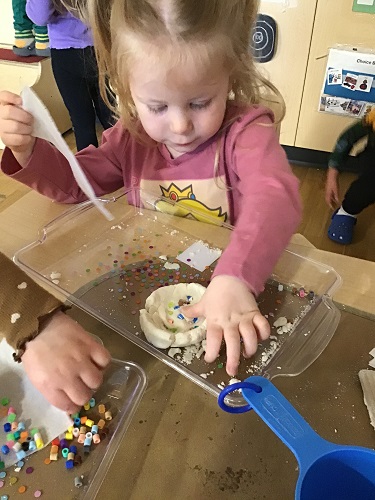 A child pushing beads into a salt dough creation