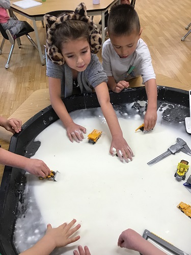 Children surrounding a tuff tray filled with oobleck and tools