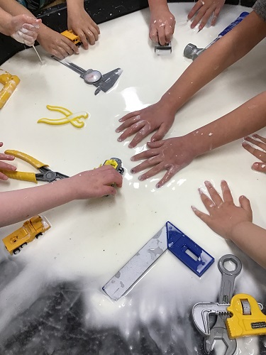 Children's hands in a sensory bin filled with oobleck and tools