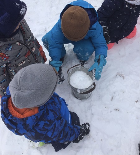 Children filling up a pail filled with snow