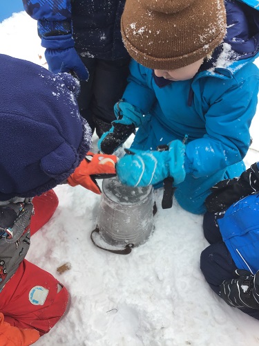 Children patting the bottom of a pail filled with snow