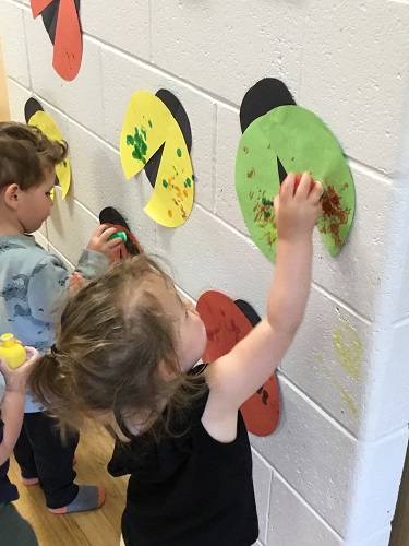Two children standing at a wall using bingo dabbers to decorate cut out ladybugs