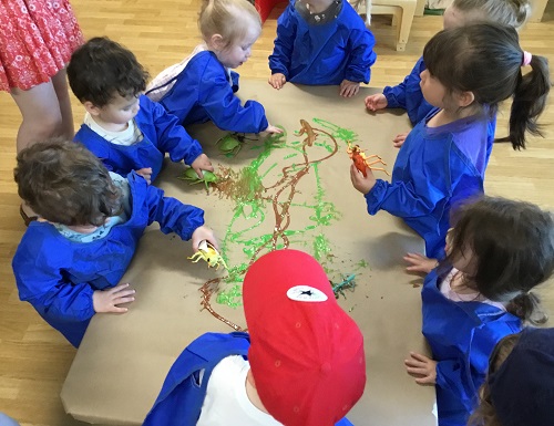 A group of children at a table painting with plastic bugs
