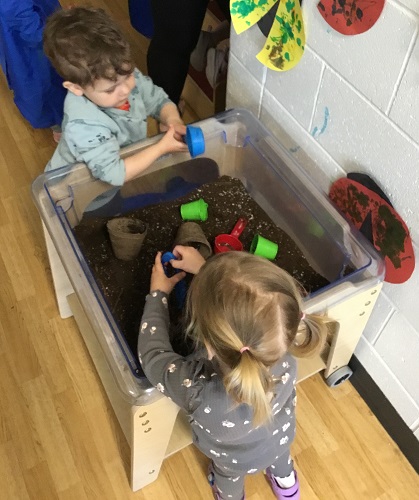 Two children standing at a sensory bin playing in soil