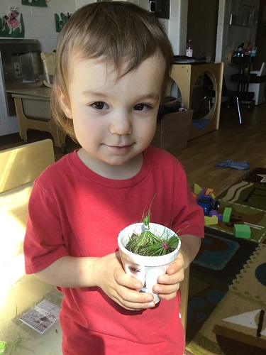 A child holding his cup with grass growing in it