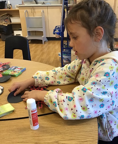A child at a table using glue on her craft