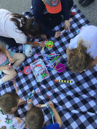 Children sitting on a table cloth outisde doing crafts