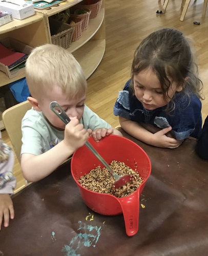 Two children at a table mixing bird seed in a bowl with a spoon