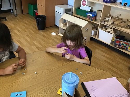 Two children at a table making their creations for Father's Day out of nuts and bolts