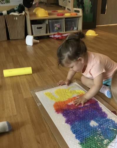 An infant touching bubble wrap covering different shades of paint