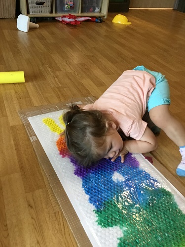 An infant laying down on the bubble wrap with paint underneath