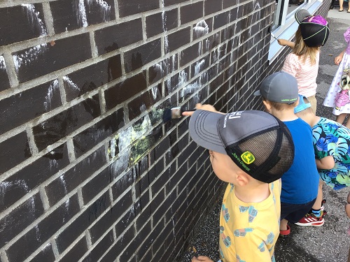 A child painting the brick wall with a paint brush 
