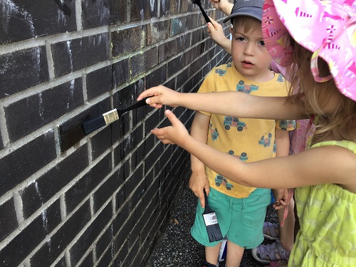 Children painting the brick wall with paint brushes 
