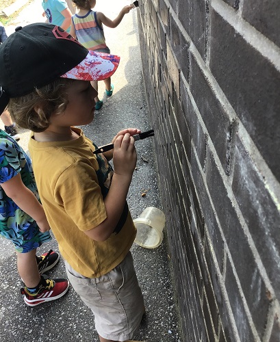 A child painting the brick wall with a paint brush 