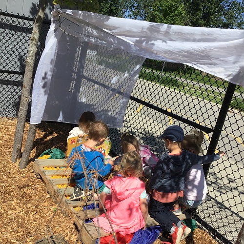 Children gathered under a canopy of tulle, sitting on pallets and blankets outside