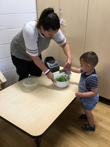 An educator and a child putting ingredients into a bowl