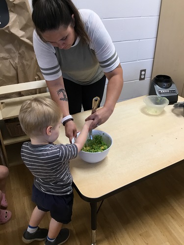 An educator helping a child stir ingredients in a bowl