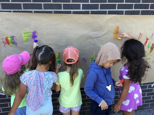 Children outside painted a large paper stuck to the wall