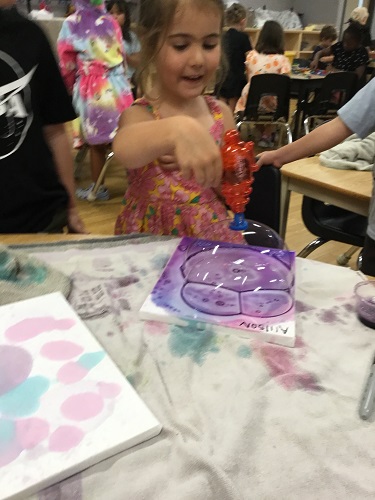 A child sitting at a table using a bubble gun to create bubbles on a canvas