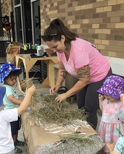 An educator and children gluing hay to a large piece of paper