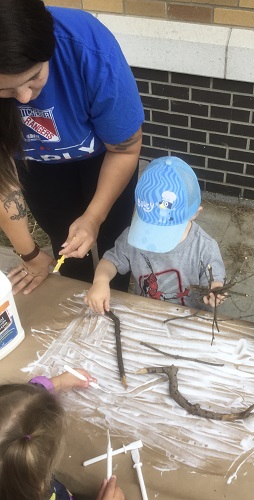 An educator and a child gluing sticks to a large piece of paper