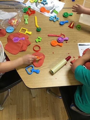 Children sitting around a table with playdough, mats and toys on the table