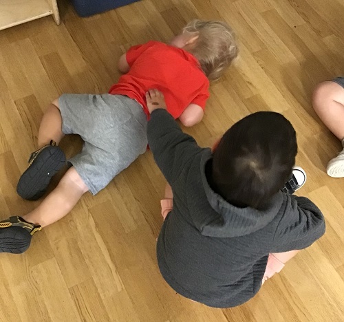 A child sitting beside another child on the floor, rubbing his back